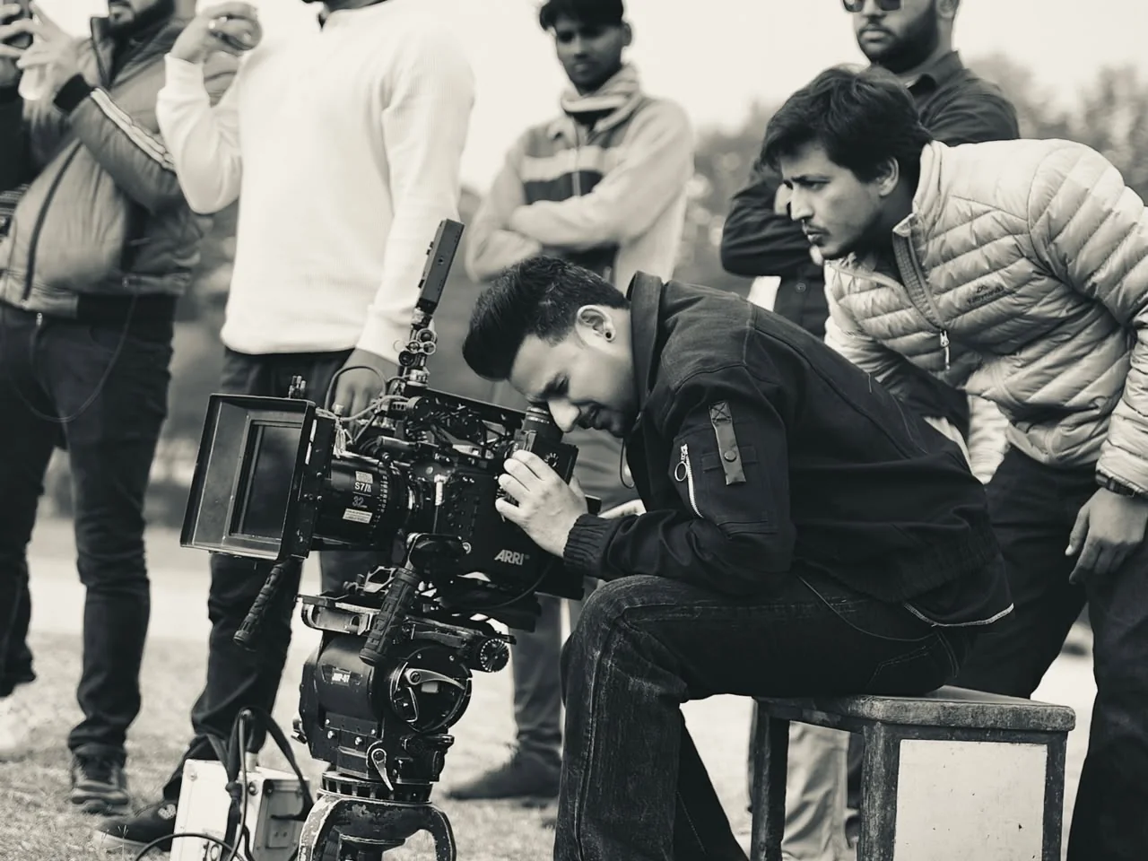 The camera operator lines up a shot on the tripod, the crew watching over his shoulder