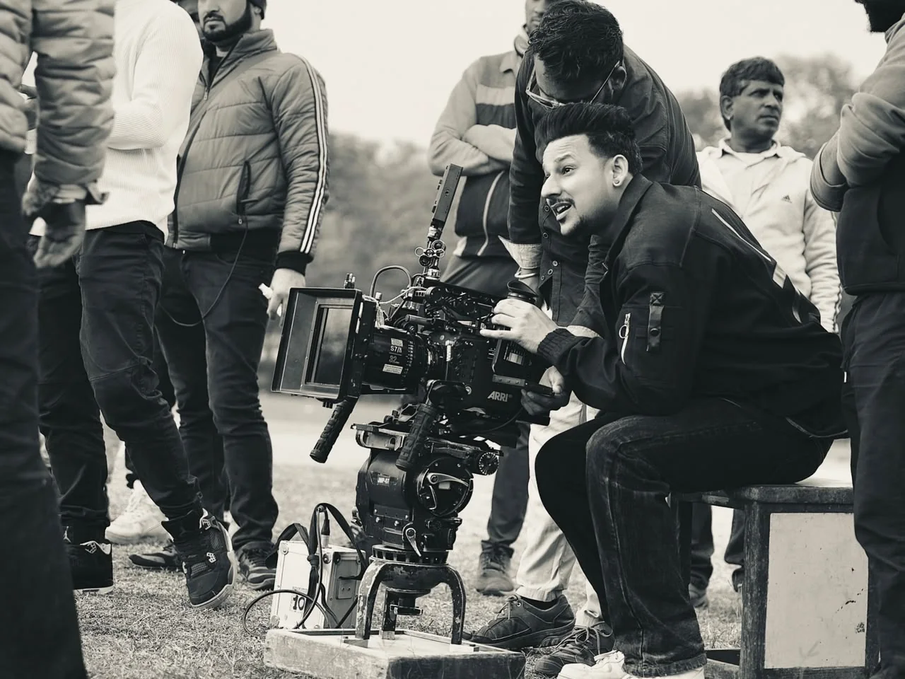 Crouched at the camera outdoors, the crew looking on